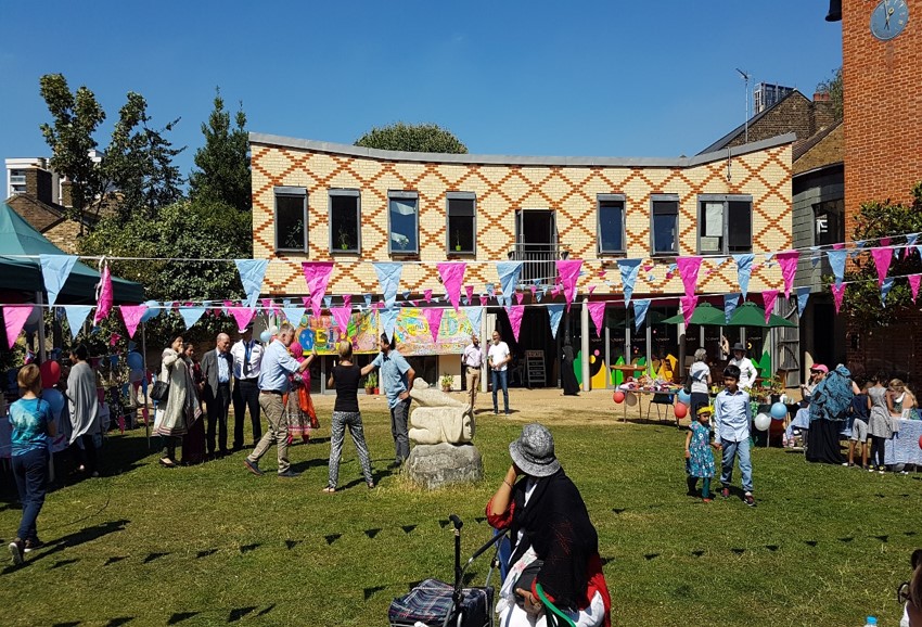Image of Bromley by Bow community hub, a building with people on the grass outside. Bunting is hung across the space where an event is happening.